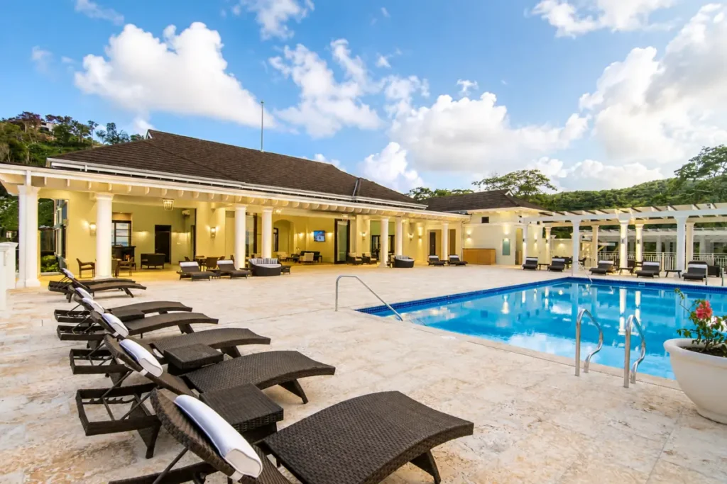 Outdoor club pool deck with wicker loungers, tiled terrace and clubhouse under a blue sky