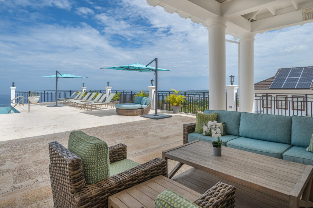 Ocean-view pool terrace with lounge seating, turquoise umbrellas, and white columns