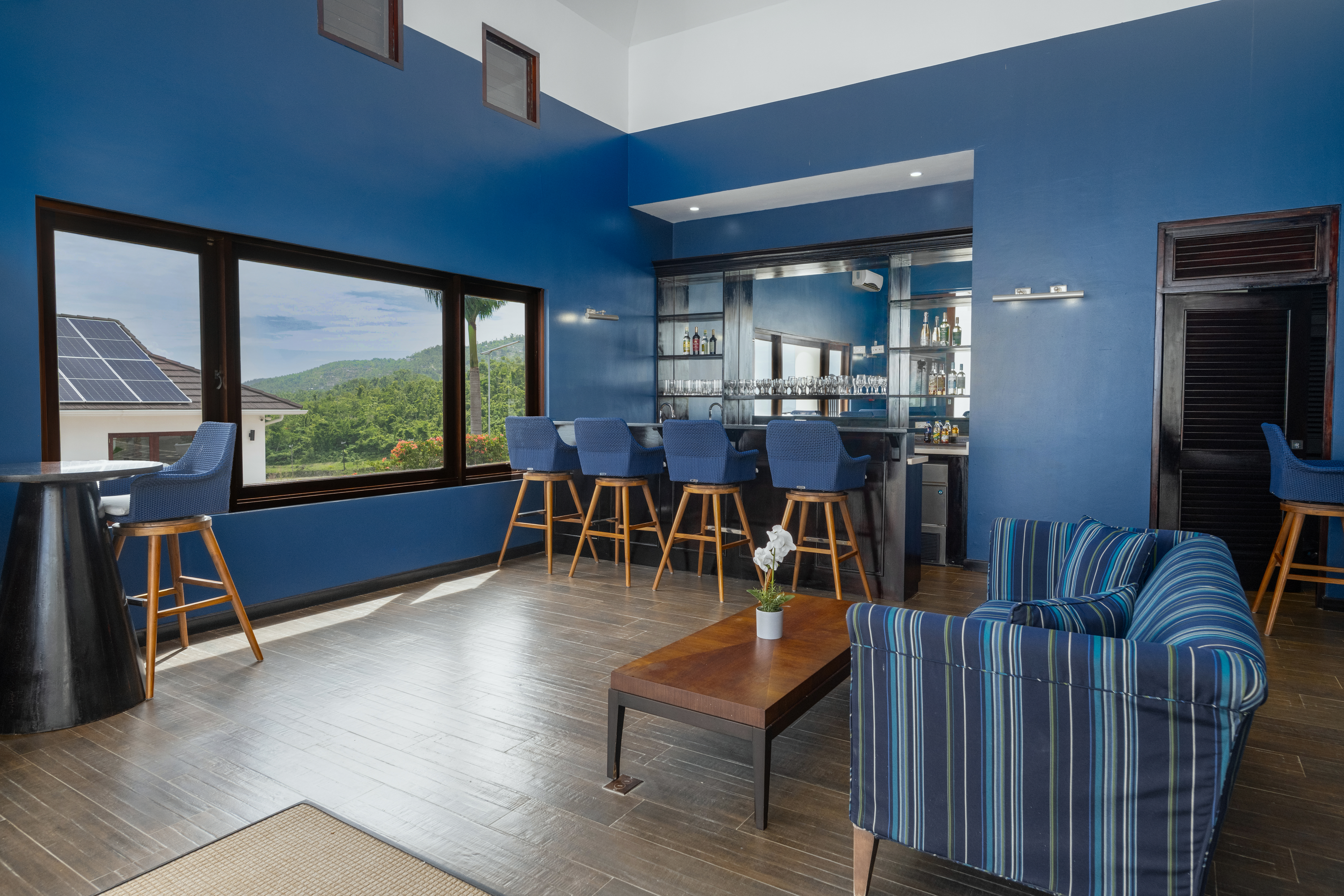 Interior clubhouse lounge with blue walls, bar counter, high stools and striped armchairs