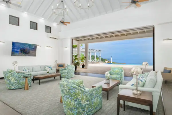 Bright coastal clubhouse lounge with vaulted white ceiling, patterned blue-green armchairs, and ocean view