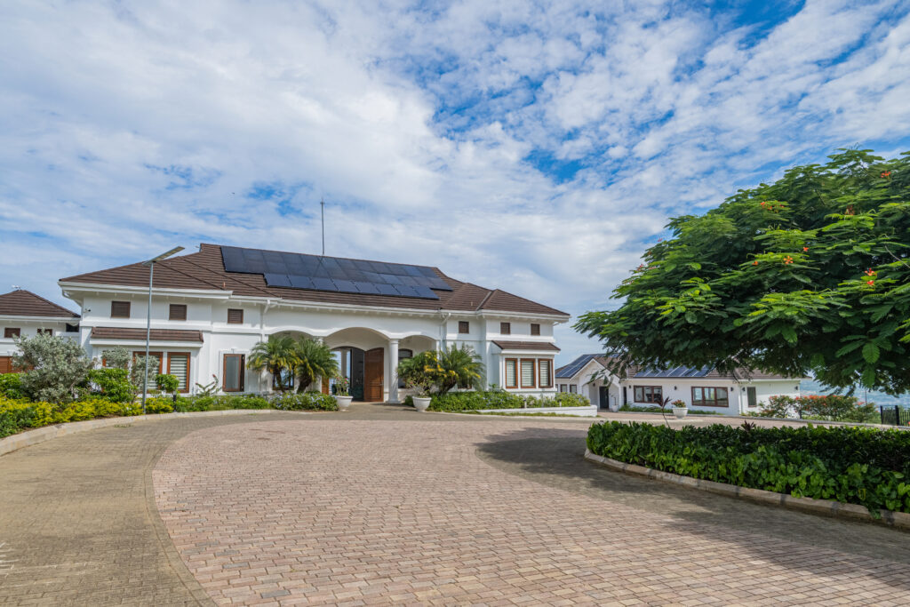 White clubhouse with rooftop solar panels, landscaped driveway and large tree under a partly cloudy sky